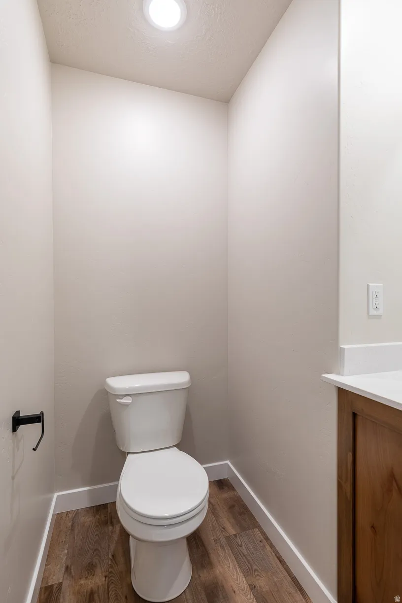 Compact bathroom featuring a white toilet, recessed ceiling light, wood-finish flooring, and white baseboards