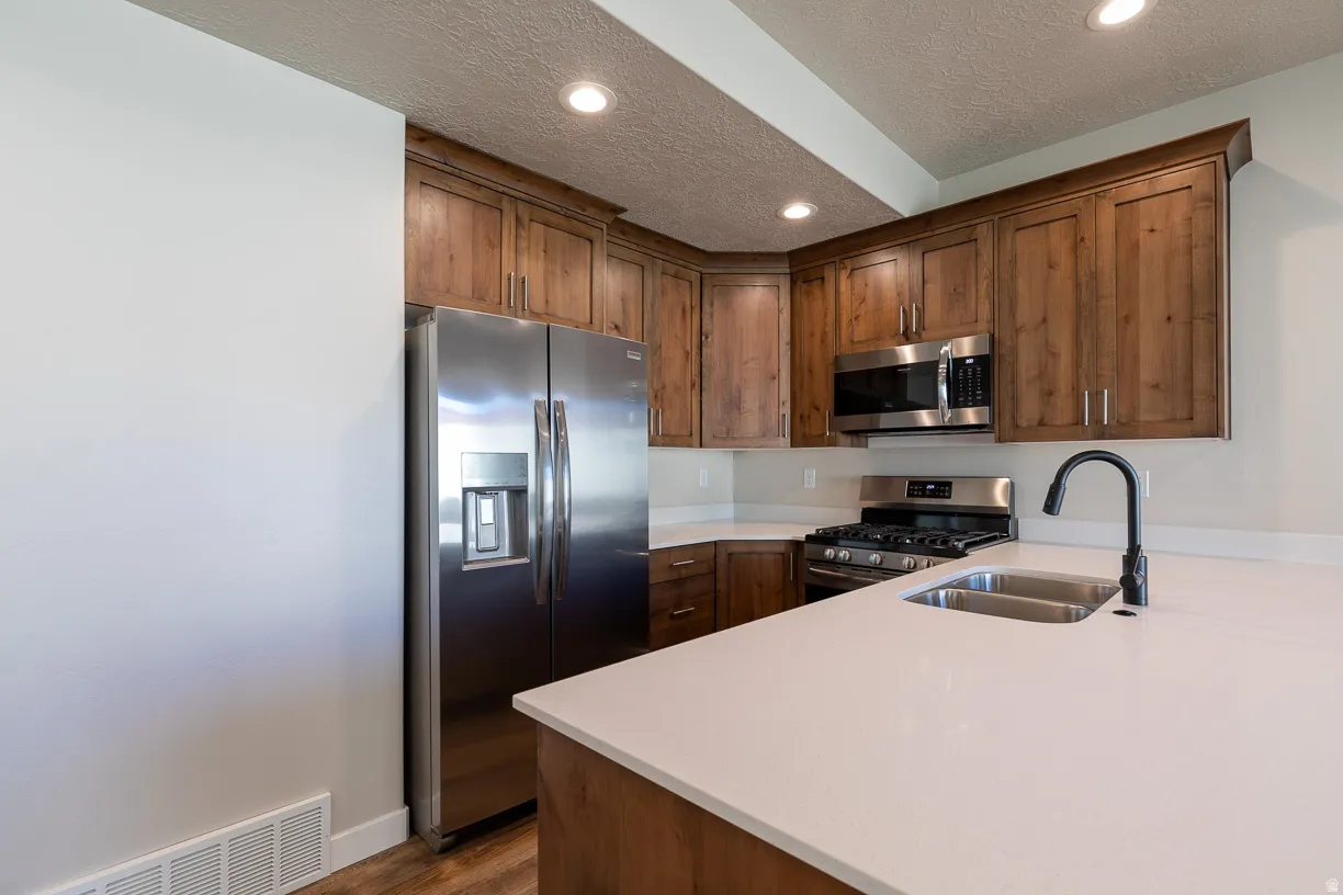 Kitchen featuring wood cabinetry, stainless steel appliances, white countertops, a double basin sink with a matte black faucet, and recessed lighting
