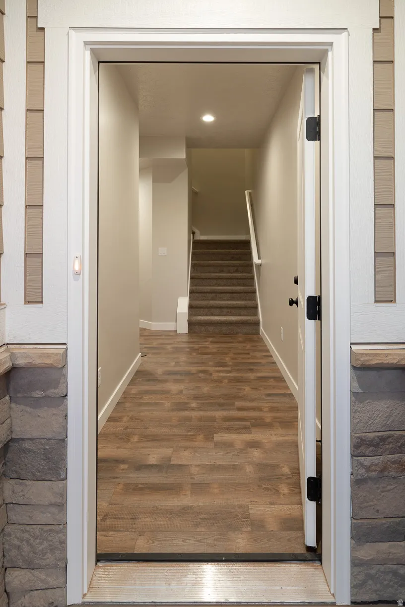 Entryway featuring wood-finish flooring extending into the hallway, a staircase with carpeted treads and white handrail, recessed ceiling lighting, and a neutral wall color palette
