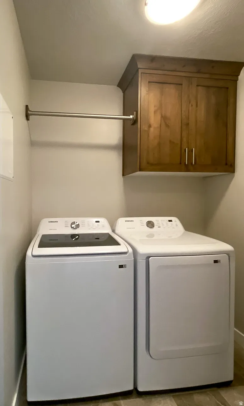 Dedicated laundry space featuring a wood-finish overhead cabinet, a chrome hanging rod, and wood-finish flooring