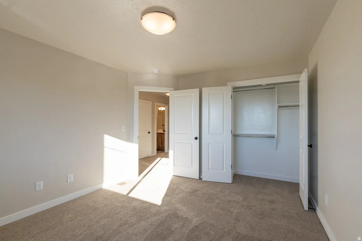 Upstairs carpeted bedroom featuring neutral wall tones, a ceiling-mounted light fixture and spacious closet.