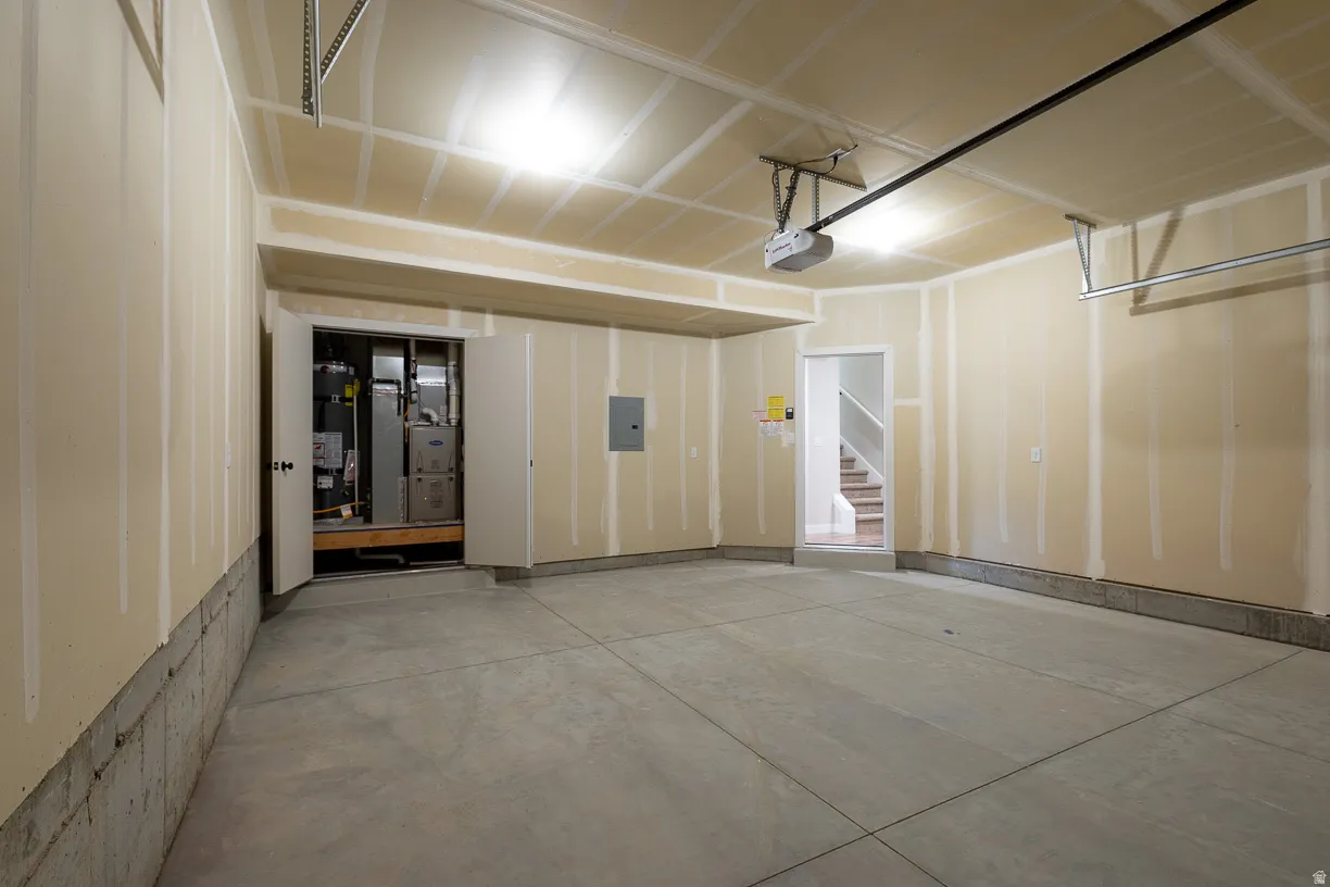 Spacious two car garage with a concrete floor, exposed drywall, overhead lighting, utility room, and direct entrance into the townhome.