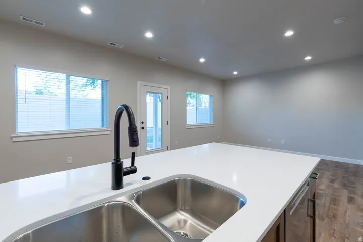 Kitchen island featuring a double basin stainless steel sink with a matte black gooseneck faucet, white solid surface countertop, and wood-finish cabinetry