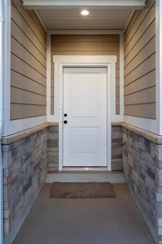 Covered porch entry featuring a white panel door with dark hardware, recessed lighting, and a composite siding exterior with stone veneer accents