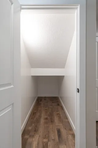 Under-stair storage area featuring wood-finish flooring, white baseboards, and a built-in shelf