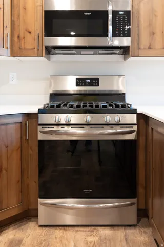 Stainless steel range with a built-in microwave, complemented by wood cabinetry, light-toned countertops, and wood-finish flooring