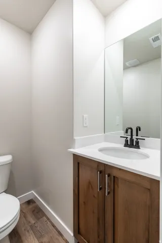 Powder room featuring a wood-finish vanity with a white countertop and undermount sink, matte black faucet, wall-mounted mirror, and wood-finish flooring