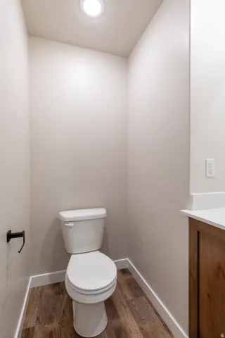 Compact bathroom featuring a white toilet, recessed ceiling light, wood-finish flooring, and white baseboards