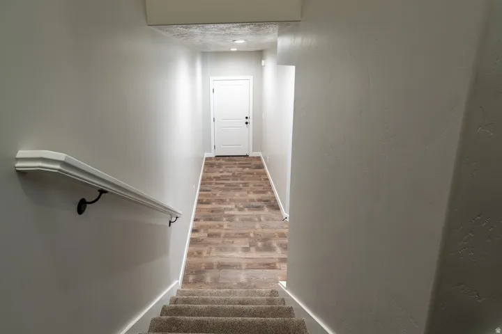Staircase featuring carpeted treads, a white handrail with black brackets, and light gray walls