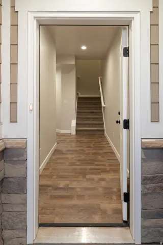 Entryway featuring wood-finish flooring extending into the hallway, a staircase with carpeted treads and white handrail, recessed ceiling lighting, and a neutral wall color palette