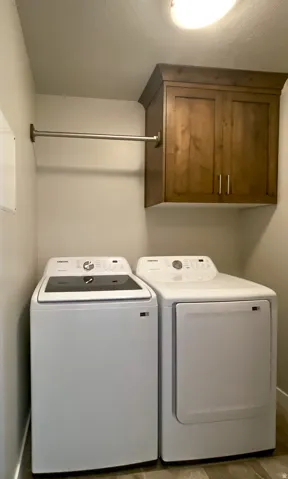 Dedicated laundry space featuring a wood-finish overhead cabinet, a chrome hanging rod, and wood-finish flooring