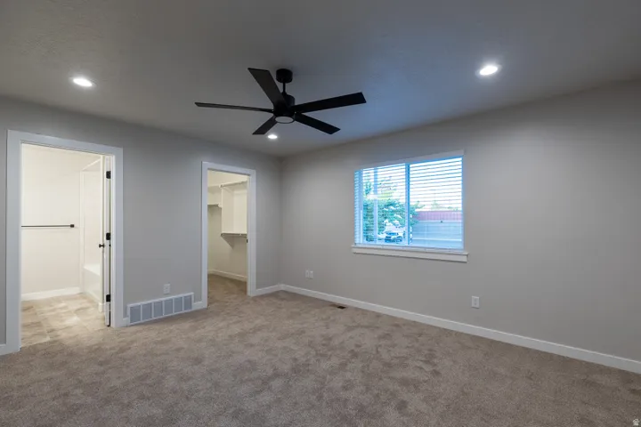 Carpeted primarybedroom featuring a black ceiling fan with integrated lighting, recessed ceiling lights, and a window with blinds
