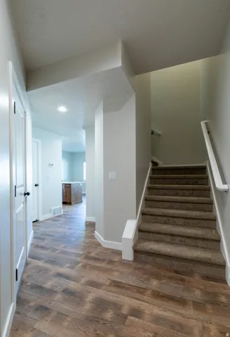 Entryway featuring wood-finish flooring, white trim, and a carpeted staircase with a white handrail