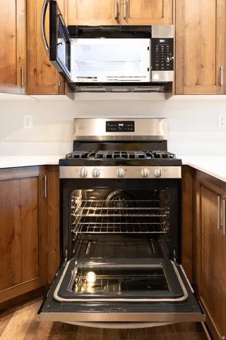 Stainless steel range with an open oven and microwave, featuring natural wood cabinetry and white countertops