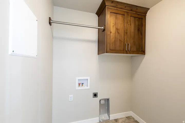 Dedicated laundry space featuring a built-in wood-finish cabinet with crown molding, a clothes hanging rod, essential hookups for a washer and dryer, and patterned floor tiling