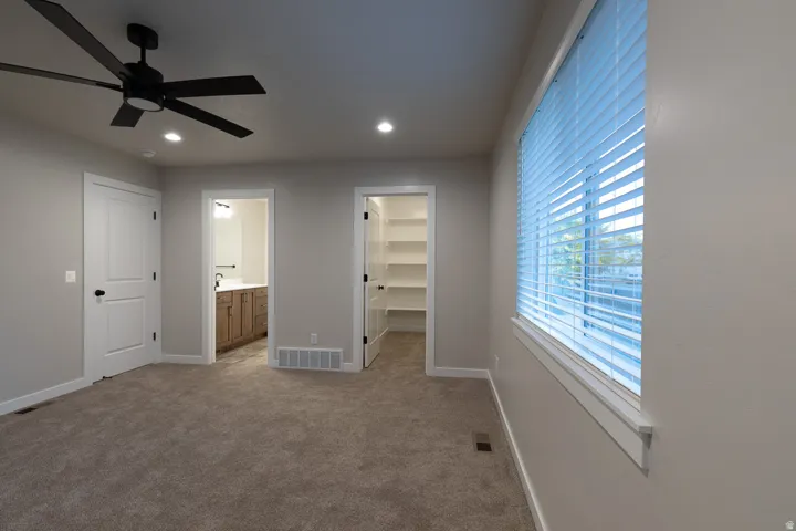Spacious carpeted primary bedroom featuring a ceiling fan, recessed lighting, and a large window with horizontal blinds