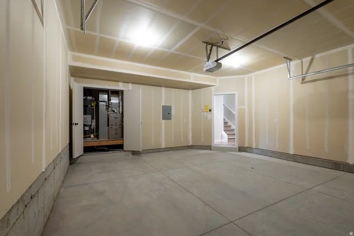 Spacious two car garage with a concrete floor, exposed drywall, overhead lighting, utility room, and direct entrance into the townhome.