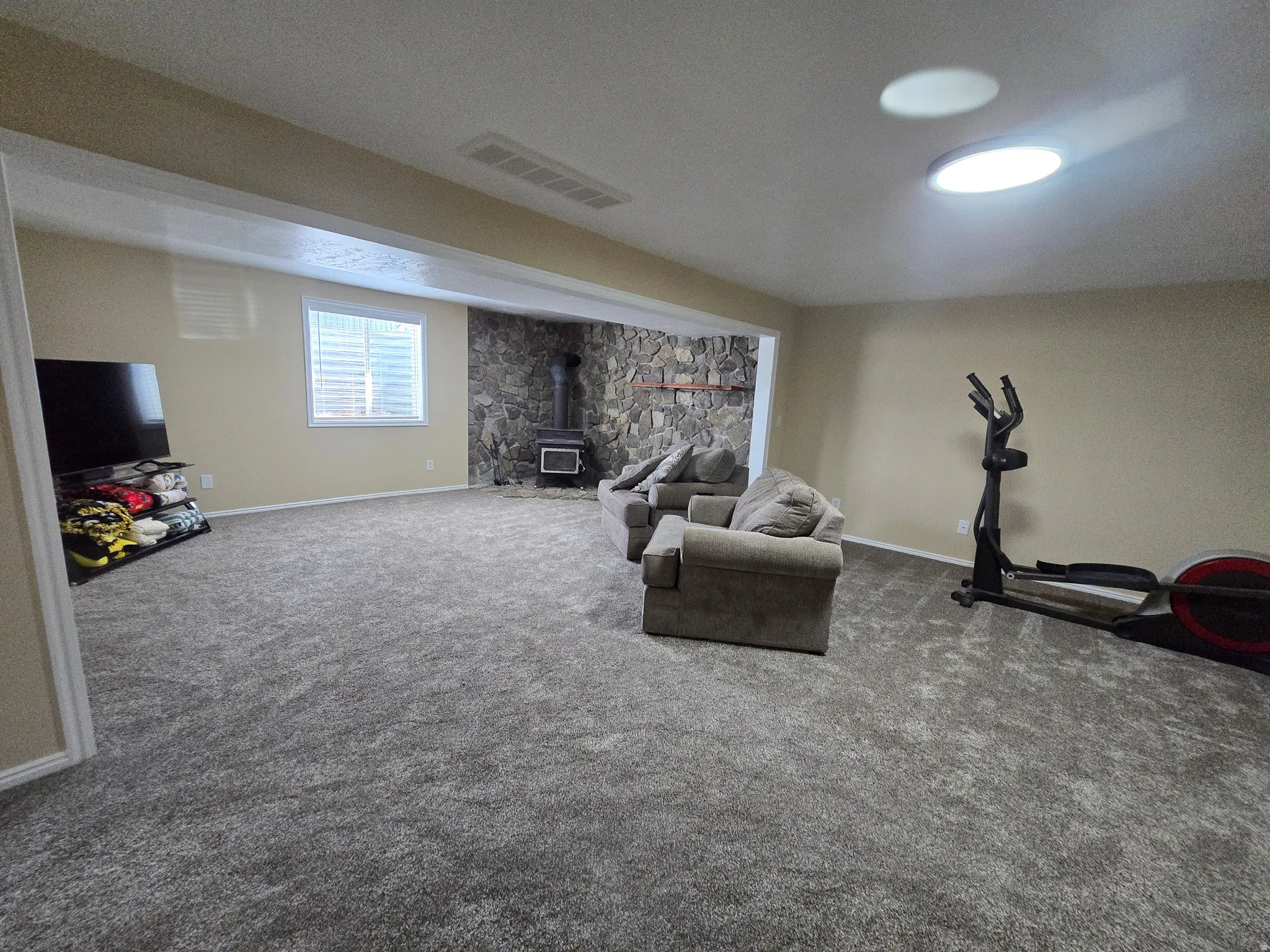 Spacious room featuring neutral carpeting, a stone accent wall, and a wood-burning stove