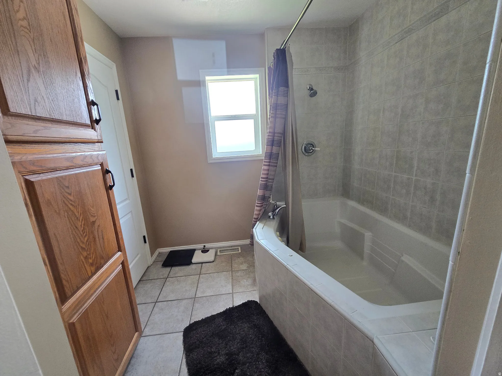 Full bathroom with a tiled tub/shower combination, window, ceramic tile flooring, and integrated wood cabinetry