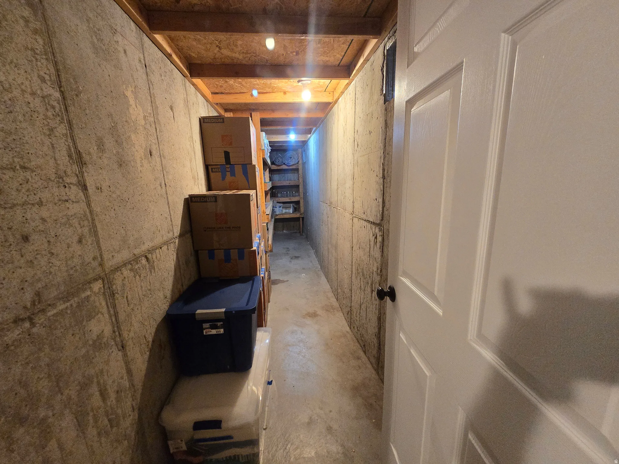 Concrete foundation walls framing a hallway with exposed wood joists and ceiling-mounted lighting