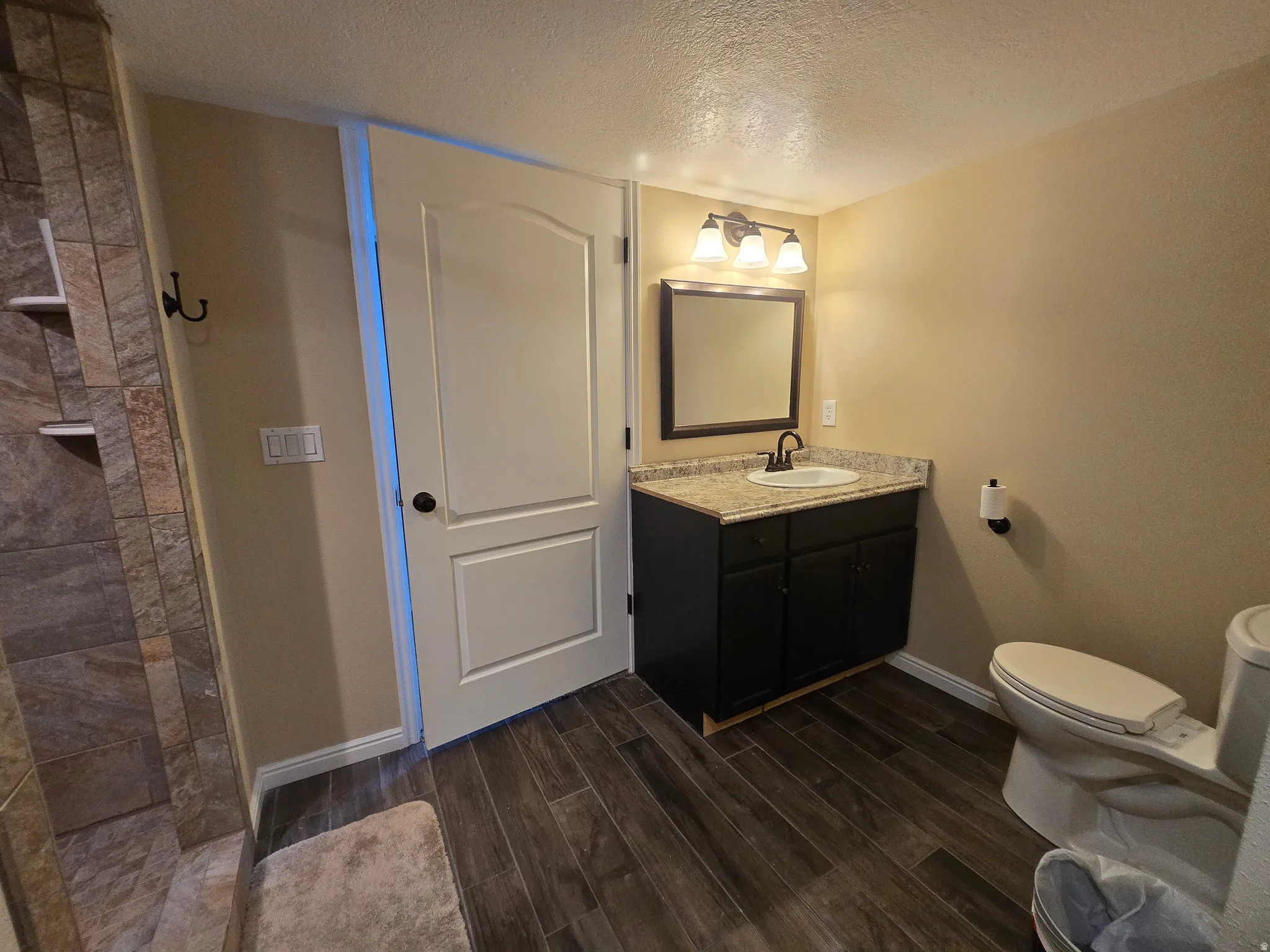 Full bathroom featuring a dark wood-finish vanity with a light-toned countertop, a rectangular mirror, and a three-light fixture