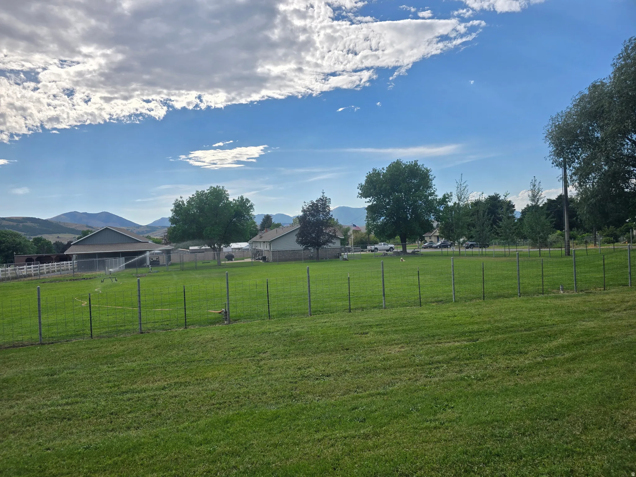 Expansive green lawn with a wire fence perimeter, backed by distant mountains and scattered trees
