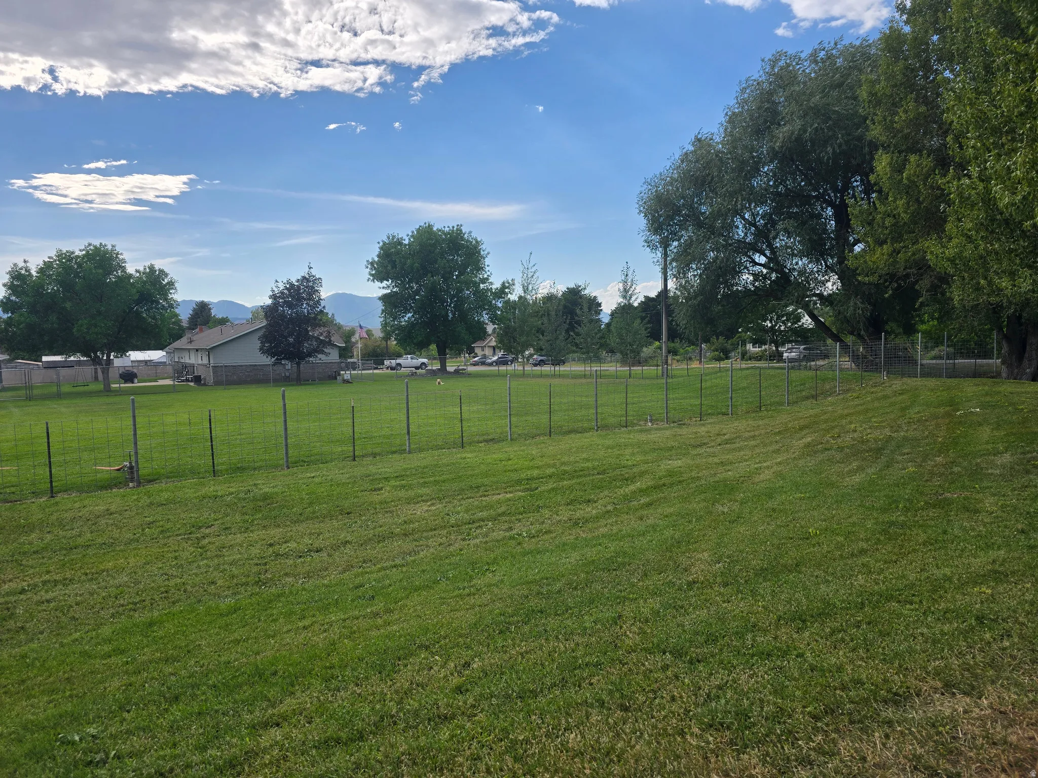 Expansive green lawn featuring a wire fence border and mature trees