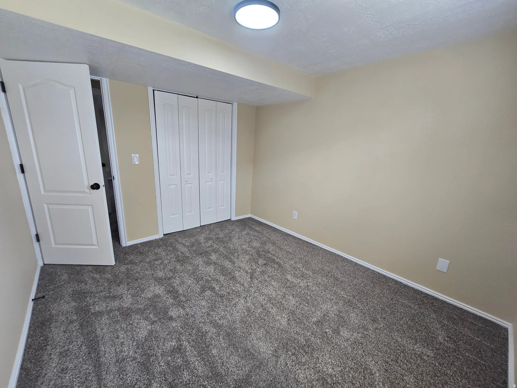 Room featuring neutral wall tones, gray carpet flooring, white bi-fold closet doors, and a flush mount ceiling light