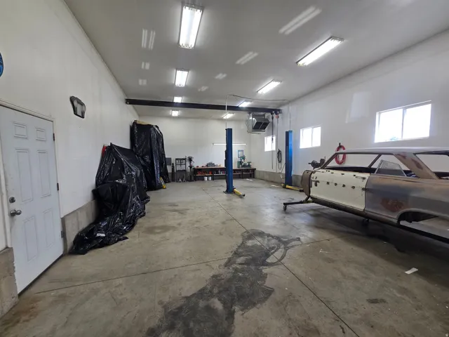 Spacious garage workshop featuring concrete flooring, multiple windows, fluorescent lighting, and a vehicle lift