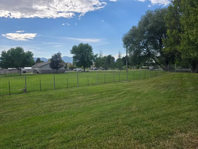 Expansive green lawn featuring a wire fence border and mature trees