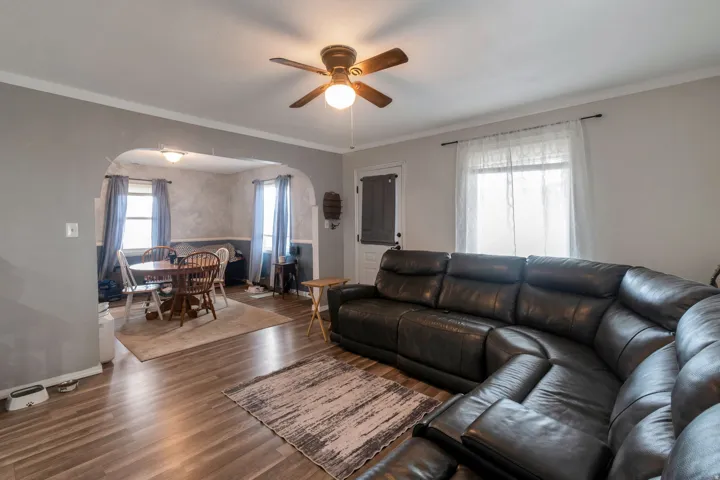 Spacious living area featuring wood-finish flooring, a ceiling fan, and crown molding