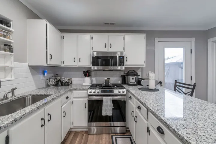 Kitchen featuring granite countertops, stainless steel appliances, white cabinetry with black hardware, white subway tile backsplash, and wood-finish flooring