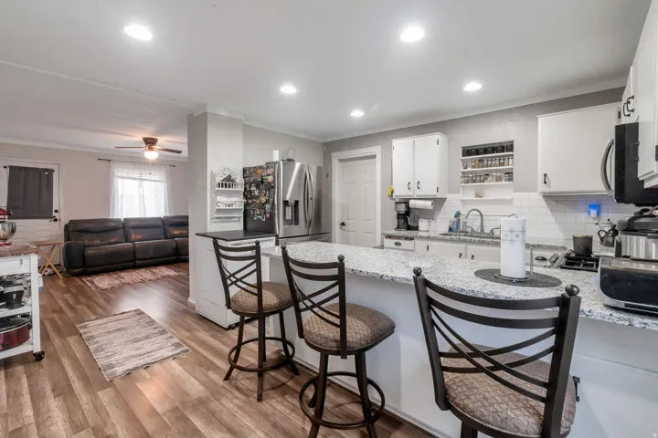 Open-concept kitchen featuring a spacious peninsula with seating, white cabinetry, integrated stainless steel appliances, and wood-finish flooring throughout