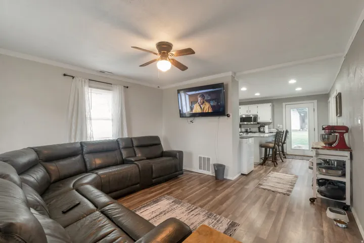 Living area featuring wood-finish flooring, a ceiling fan, and crown molding