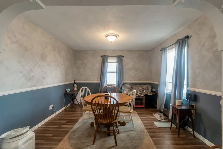 Dining area featuring wood-finish flooring, two windows with light-filtering treatments, and a decorative arched entryway