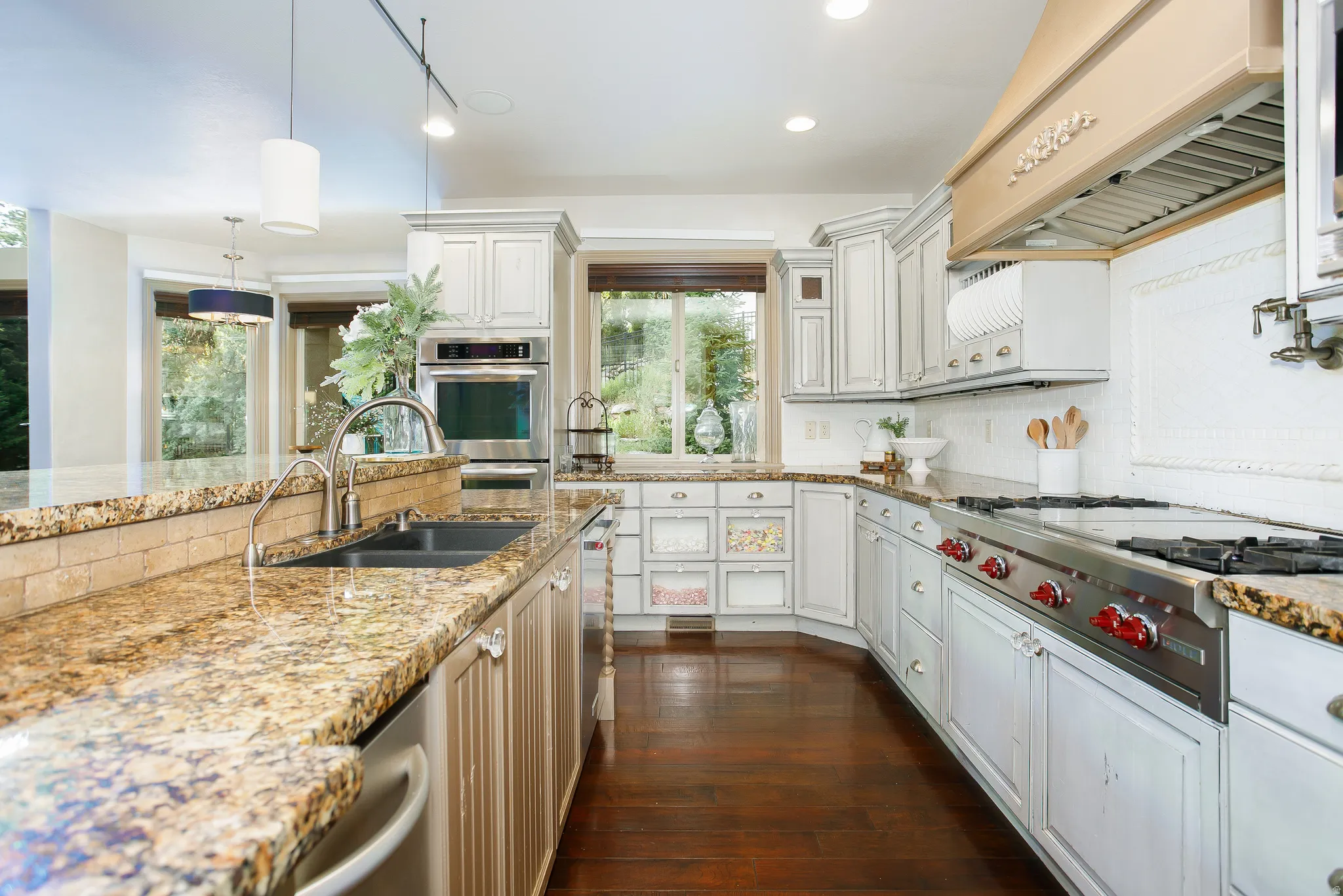 Kitchen featuring wood-finish flooring, granite countertops, white cabinetry with distressed finish, stainless steel appliances, and a decorative range hood