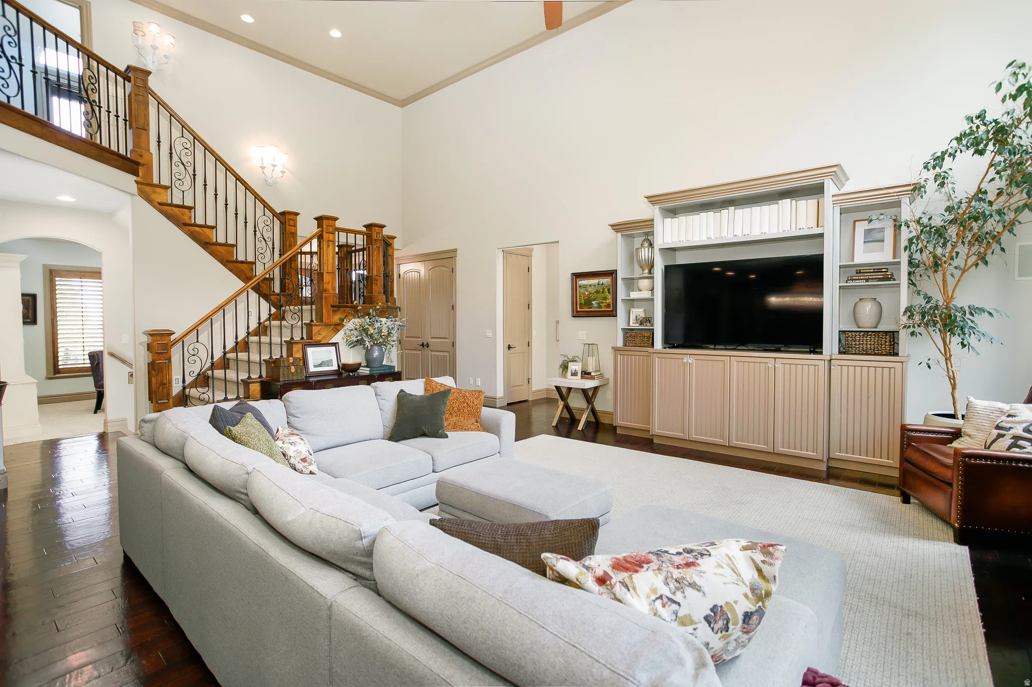 Vaulted ceiling living area featuring dark wood-finish flooring, a built-in entertainment center, and a grand staircase with wrought iron balusters and wood newel posts