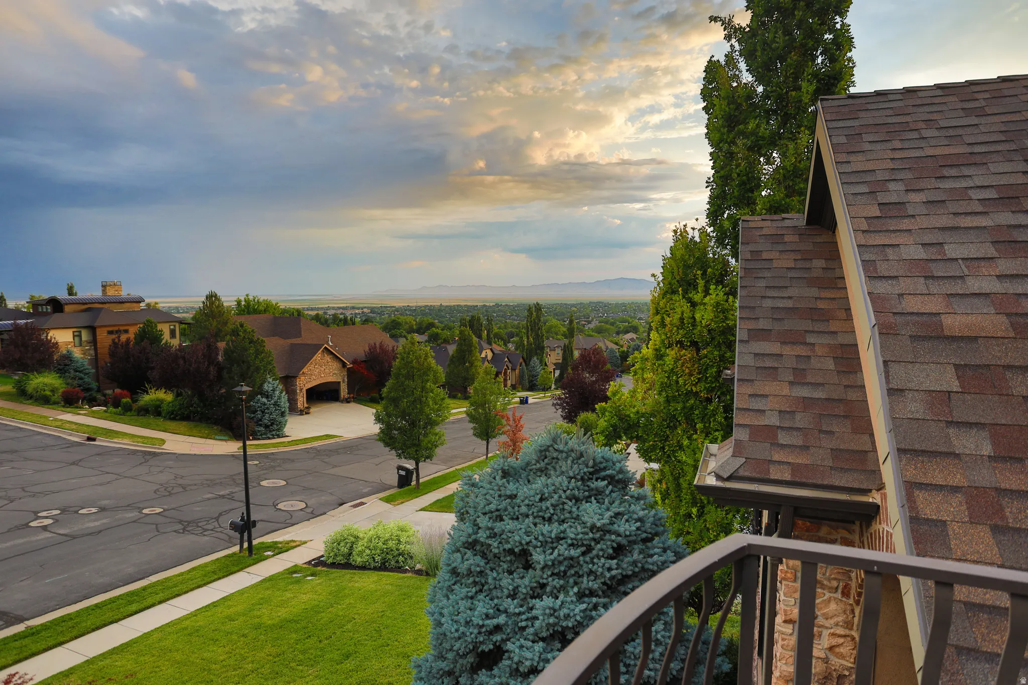 Terraced neighborhood with mature landscaping, featuring a paved street and a multi-level roofline with architectural shingles