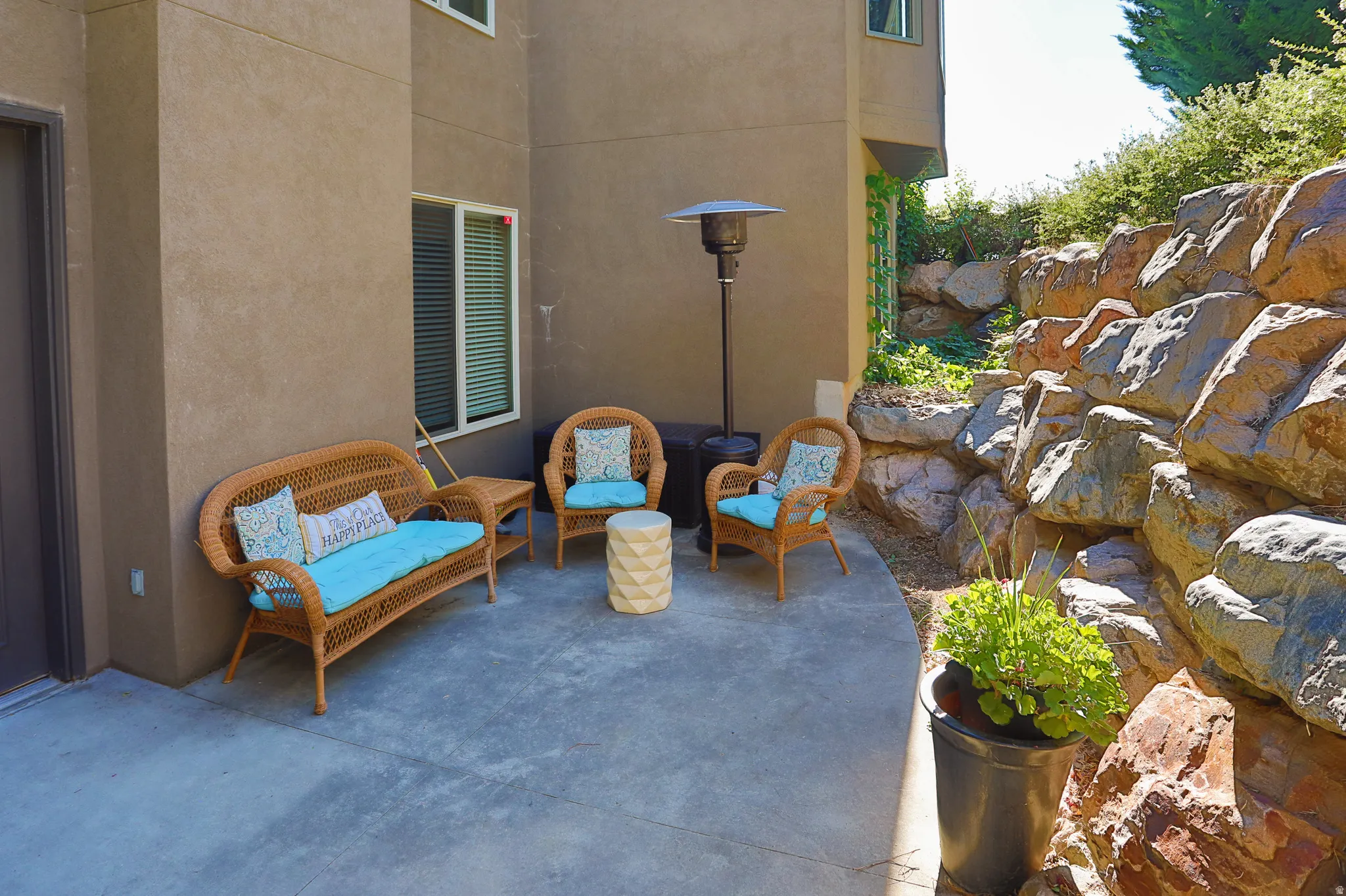 Outdoor patio featuring a concrete surface, a stucco exterior, and a rock retaining wall
