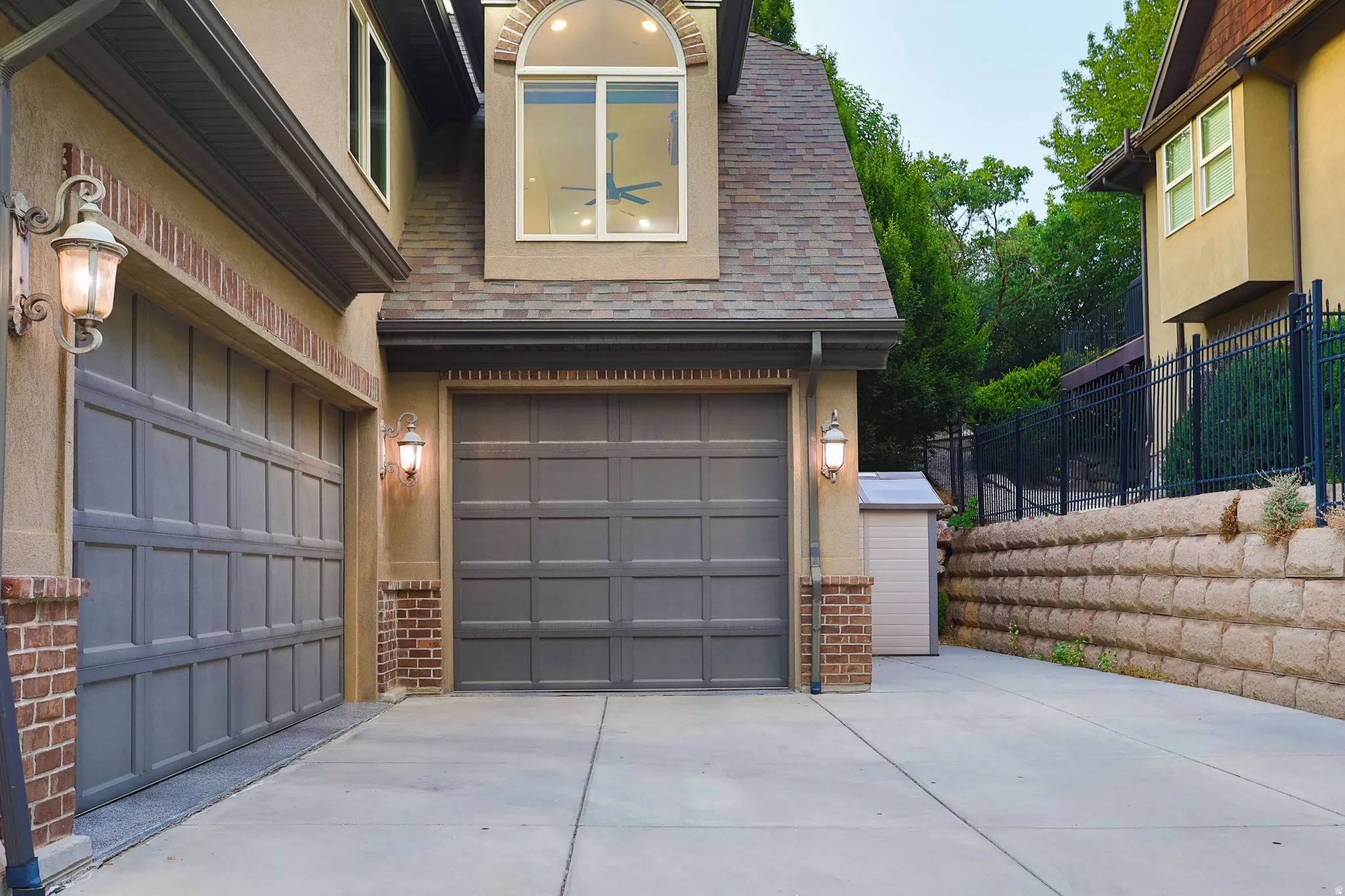 Two-car garage with panel-style doors, brick detailing, and exterior sconce lighting