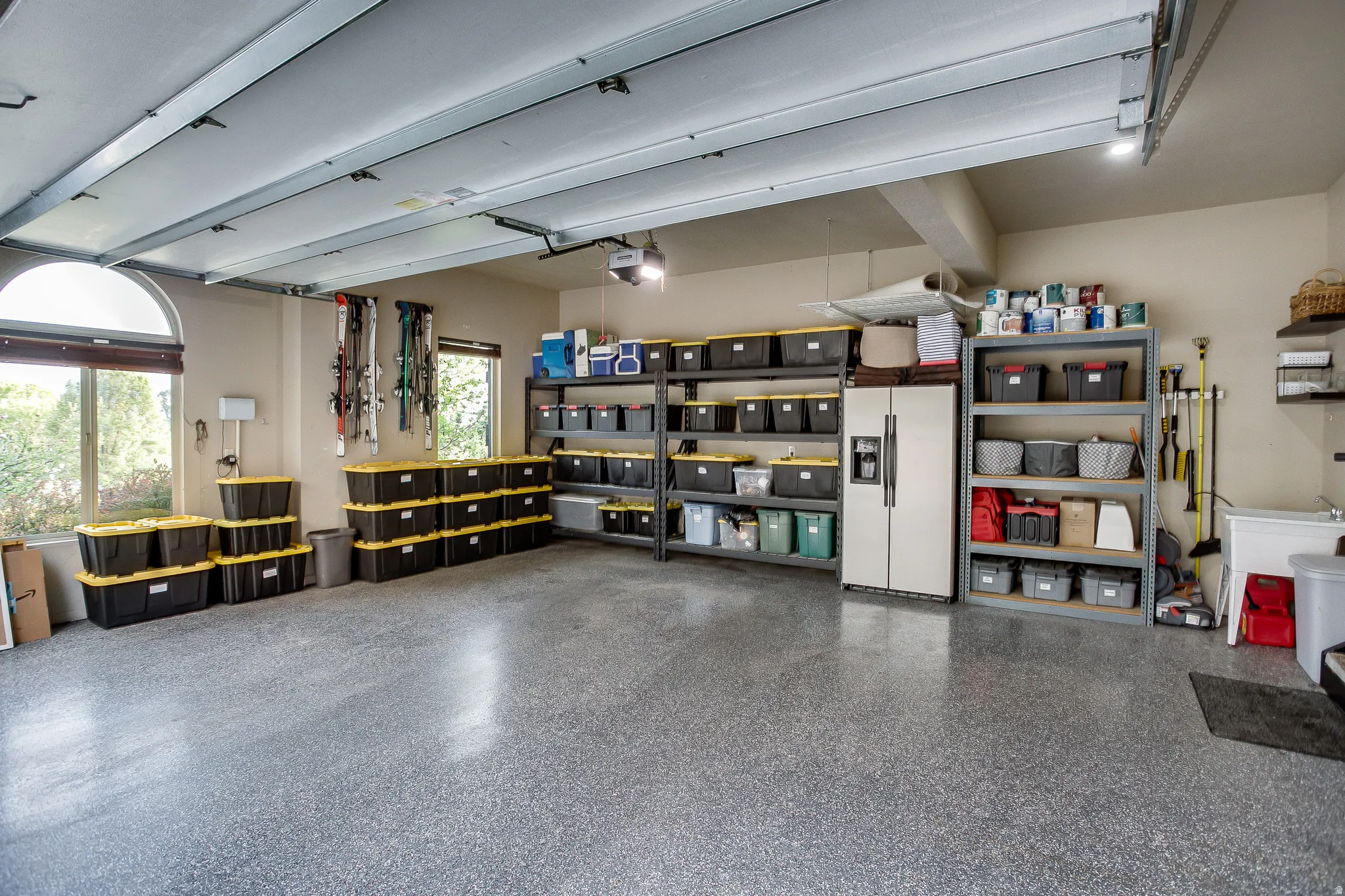 Spacious garage featuring a durable epoxy floor coating, multiple windows, recessed lighting, and extensive wall shelving for storage