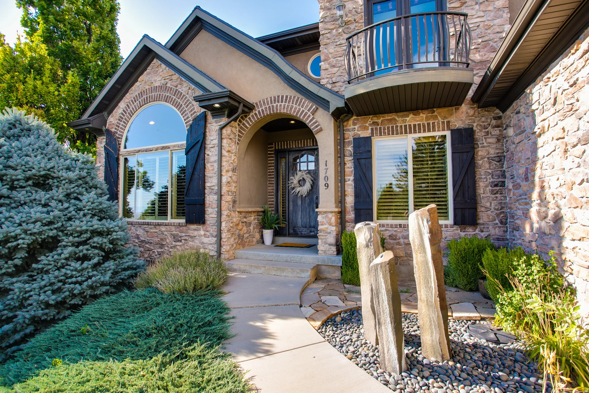 Stone and stucco exterior featuring an arched entryway, decorative balcony, and a decorative water feature with river rock