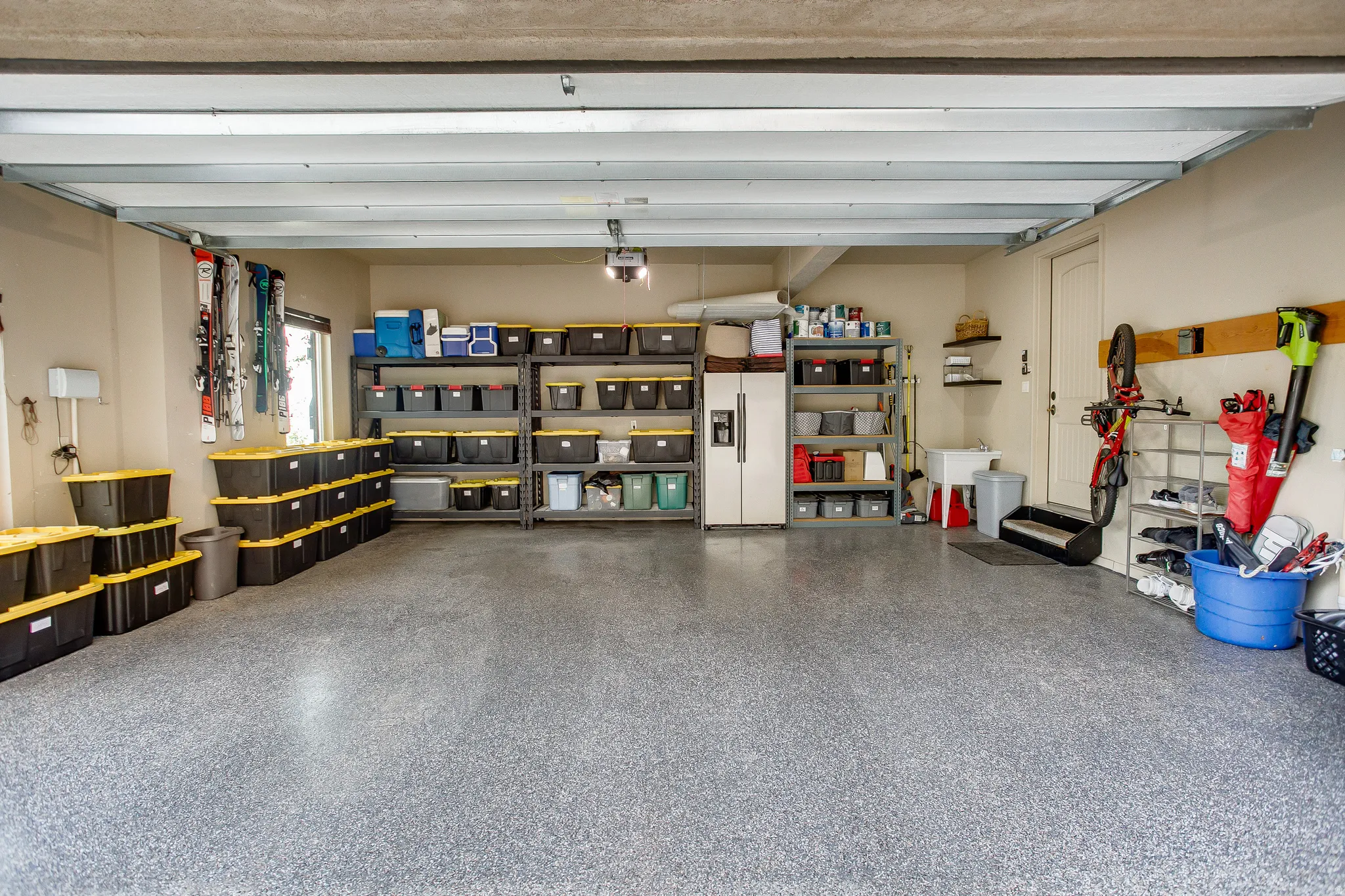 Spacious garage featuring a durable speckled epoxy floor, built-in shelving, a utility sink, and wall-mounted storage solutions