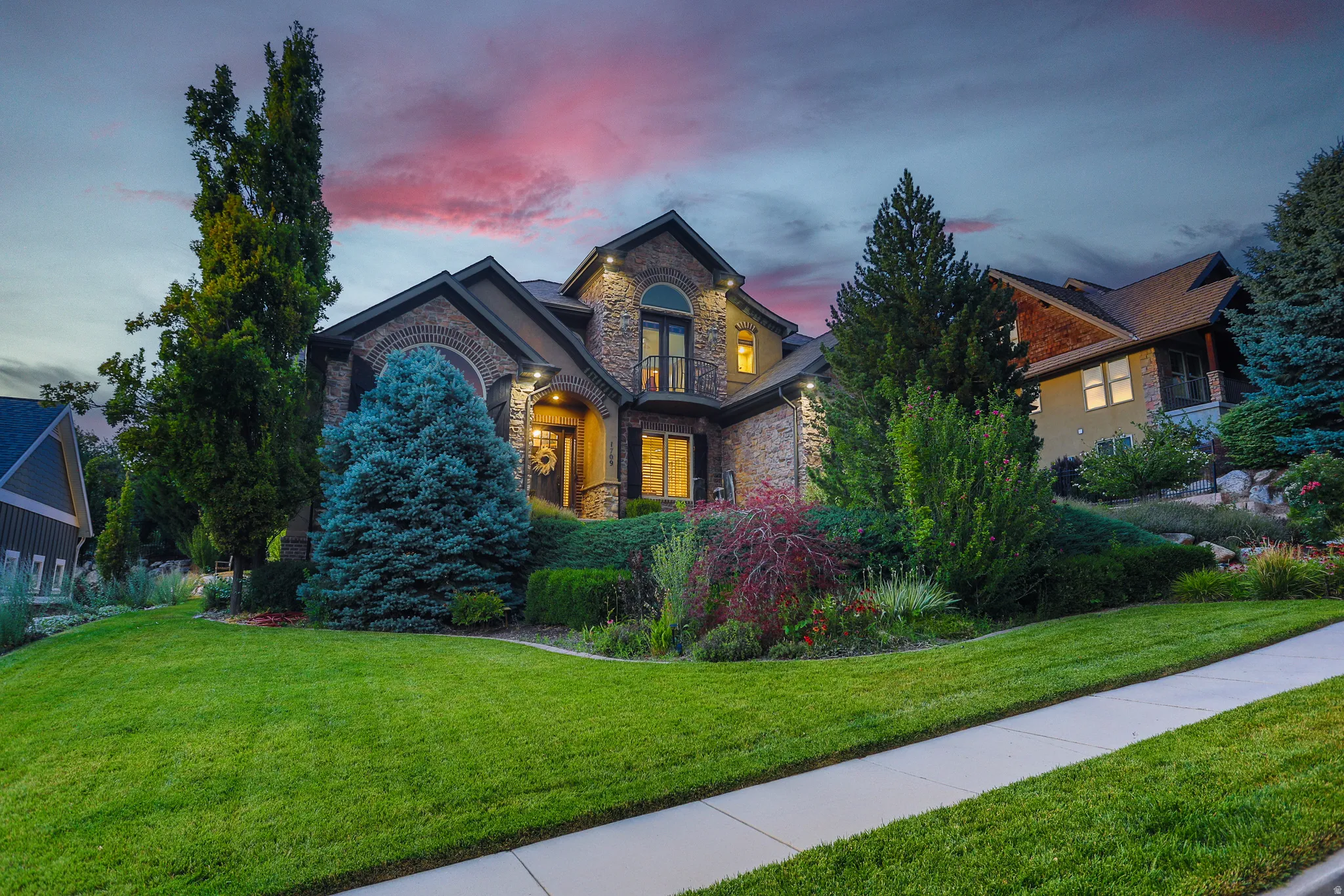 Stone and brick exterior with arched windows, prominent landscaping, and a sloped front lawn