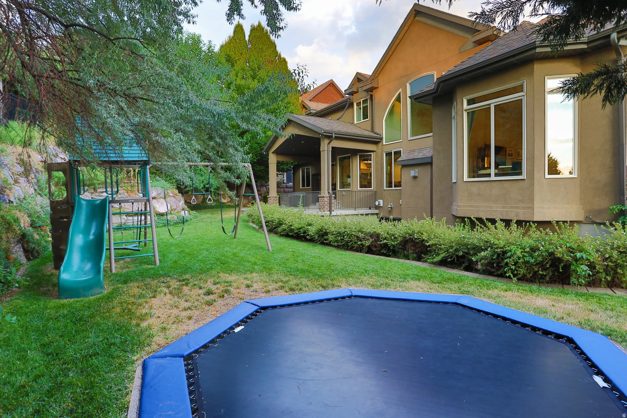 Expansive backyard featuring a manicured lawn, established trees, and a terraced rock garden