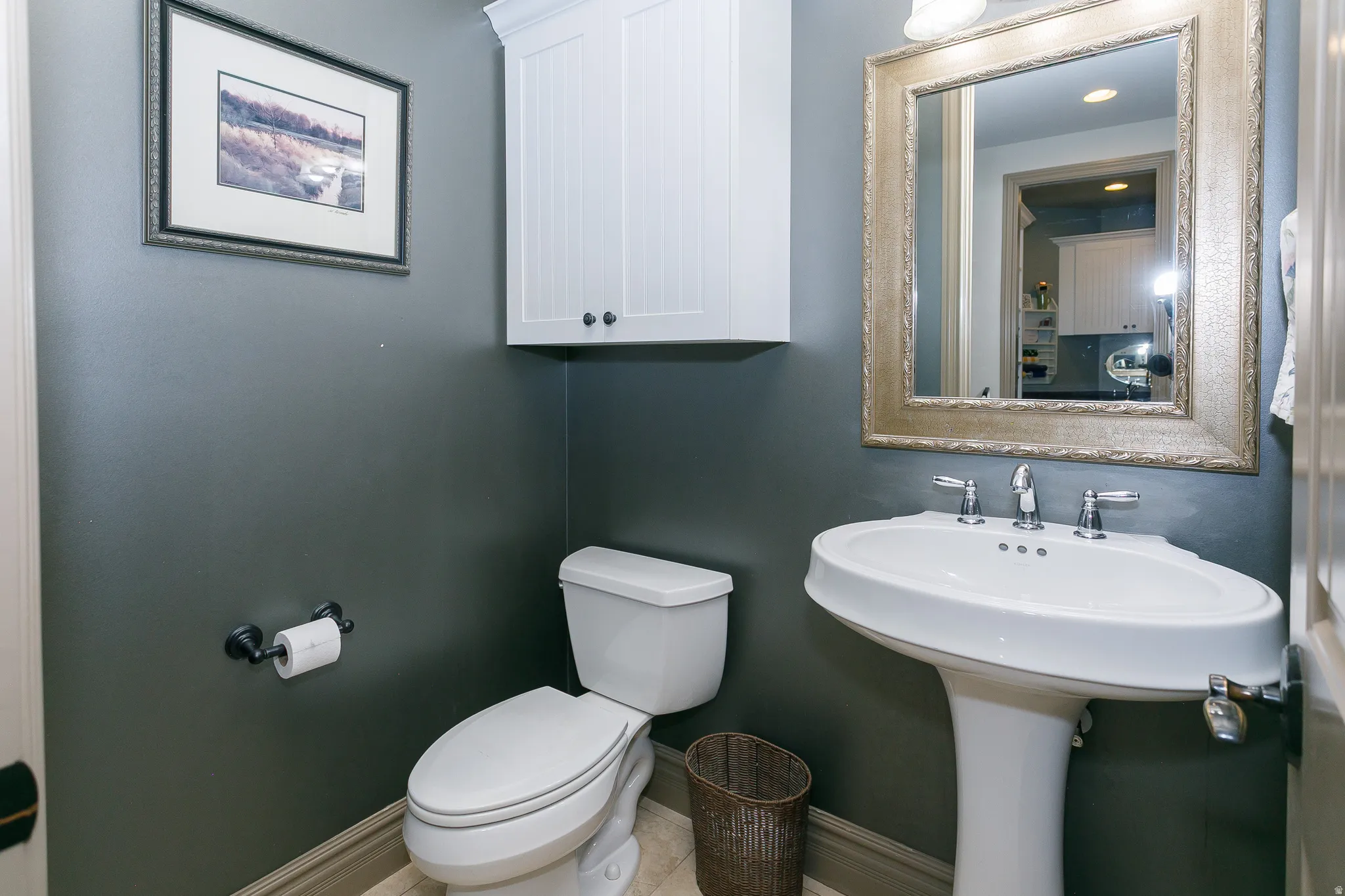 Pedestal sink with chrome faucet, complemented by a decorative framed mirror