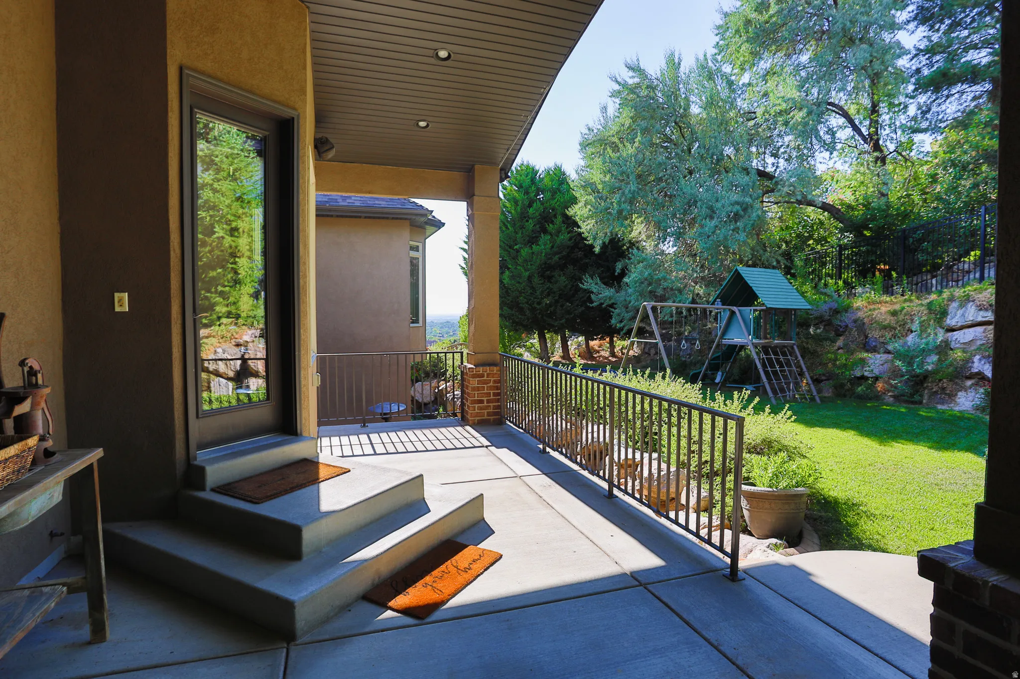 Covered patio featuring concrete flooring, a full-light exterior door, and a black metal railing