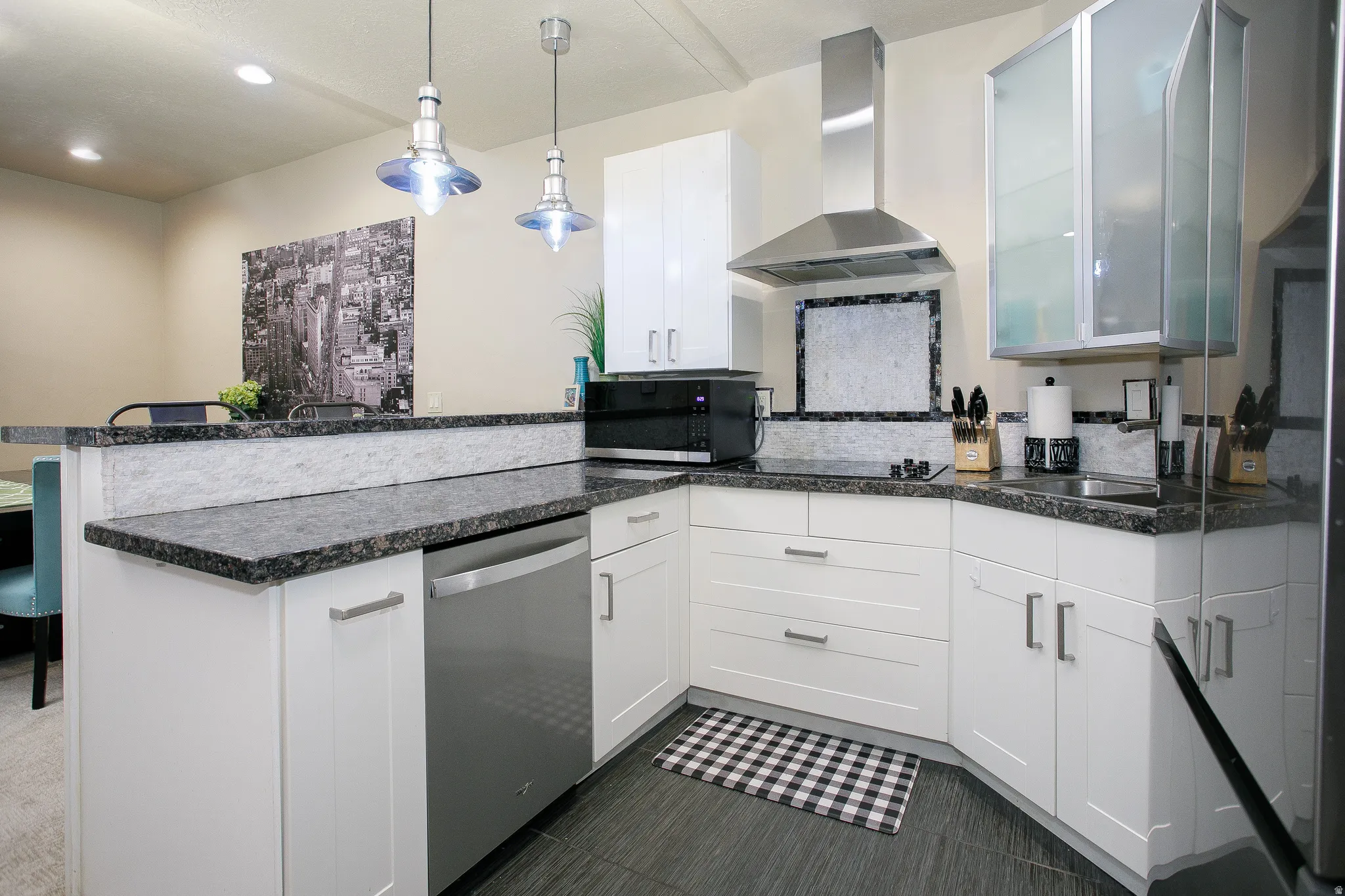 Modern kitchen featuring white cabinetry, dark granite-style countertops, stainless steel appliances, and sleek pendant lighting
