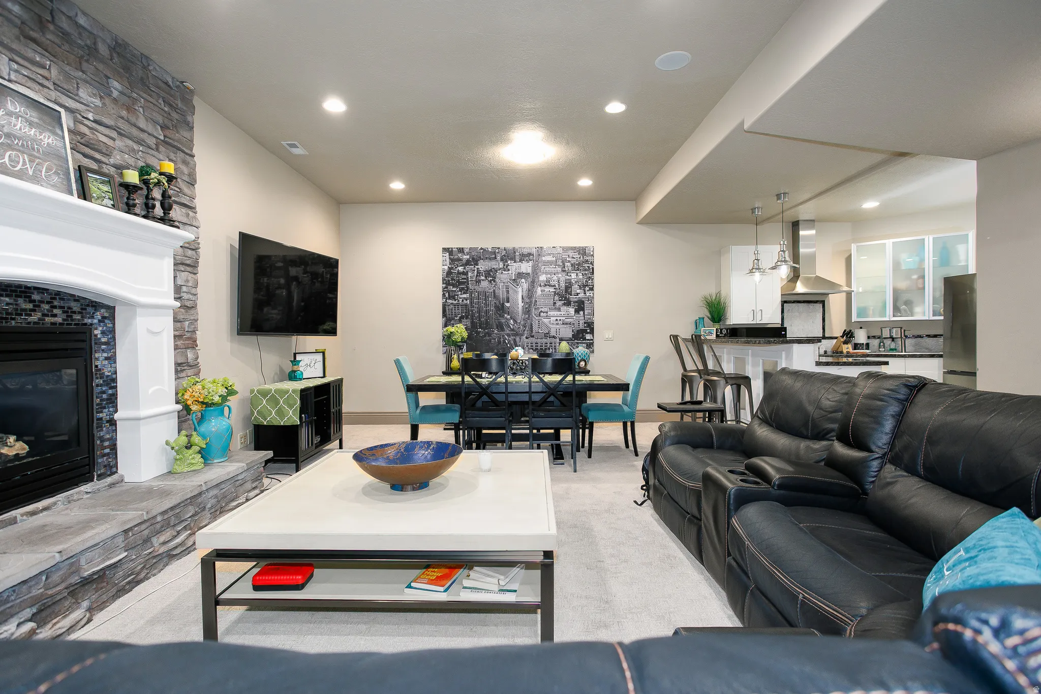 Open-concept living area featuring a stone-clad fireplace with a white mantel, recessed lighting, and light-toned carpeting