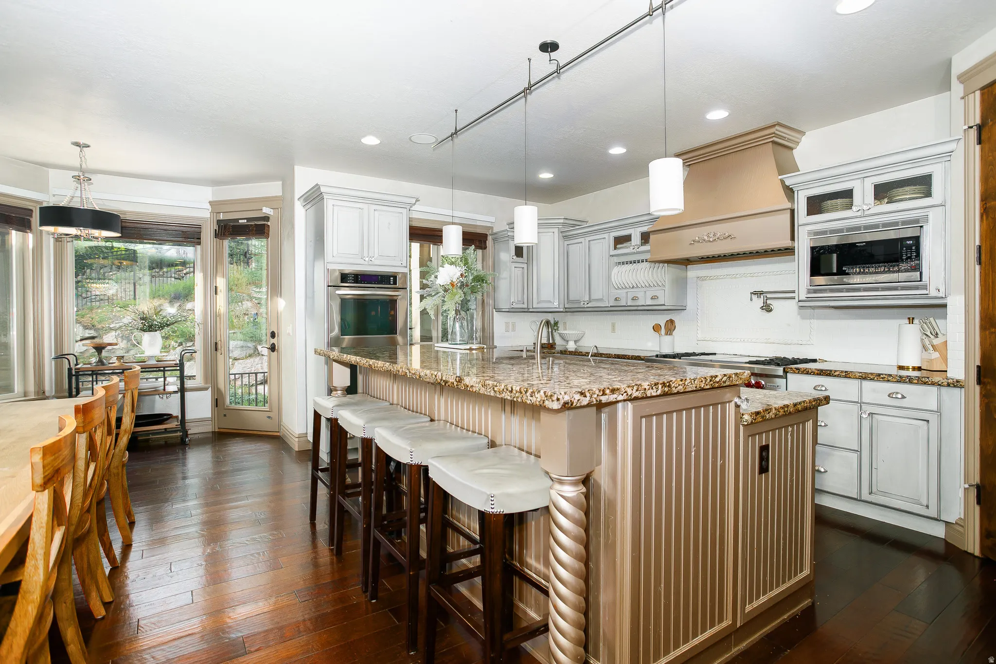 Gourmet kitchen featuring a large island with seating, granite countertops, built-in stainless steel appliances, custom cabinetry, and dark wood-finish flooring